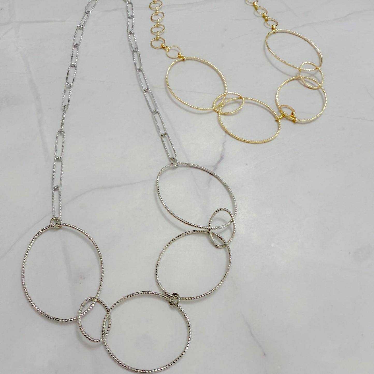 Two necklaces, one silver and one gold, on a light gray background