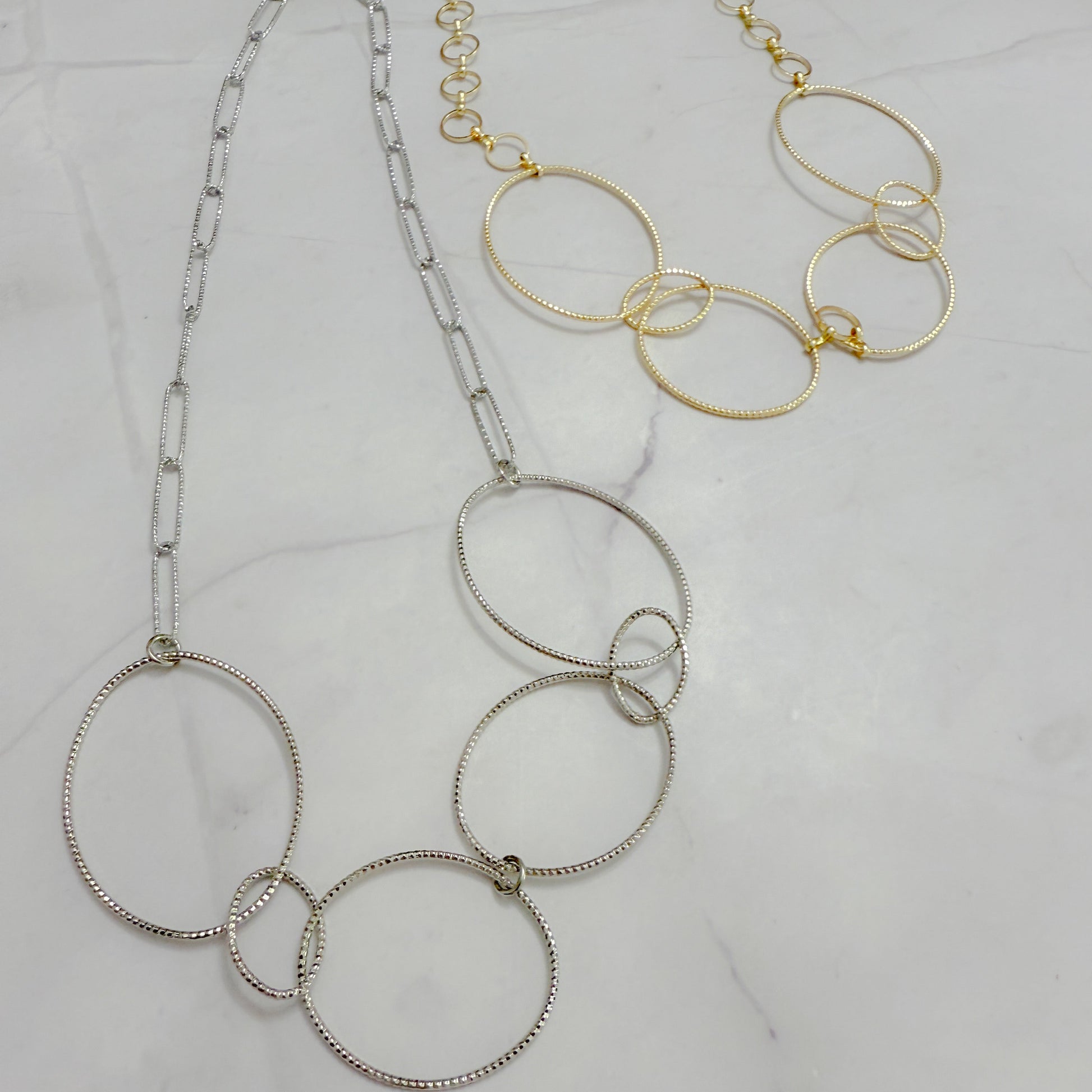 Two necklaces, one silver and one gold, on a light gray background